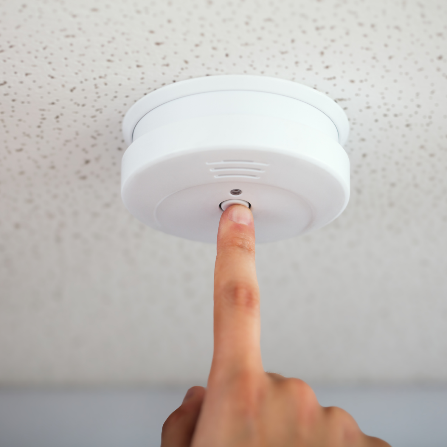 Homeowner testing smoke detector in their home